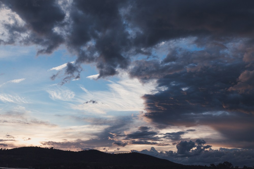 [Image Description: Stormy, cloudy sky at sunset over mountain silhouette.]
