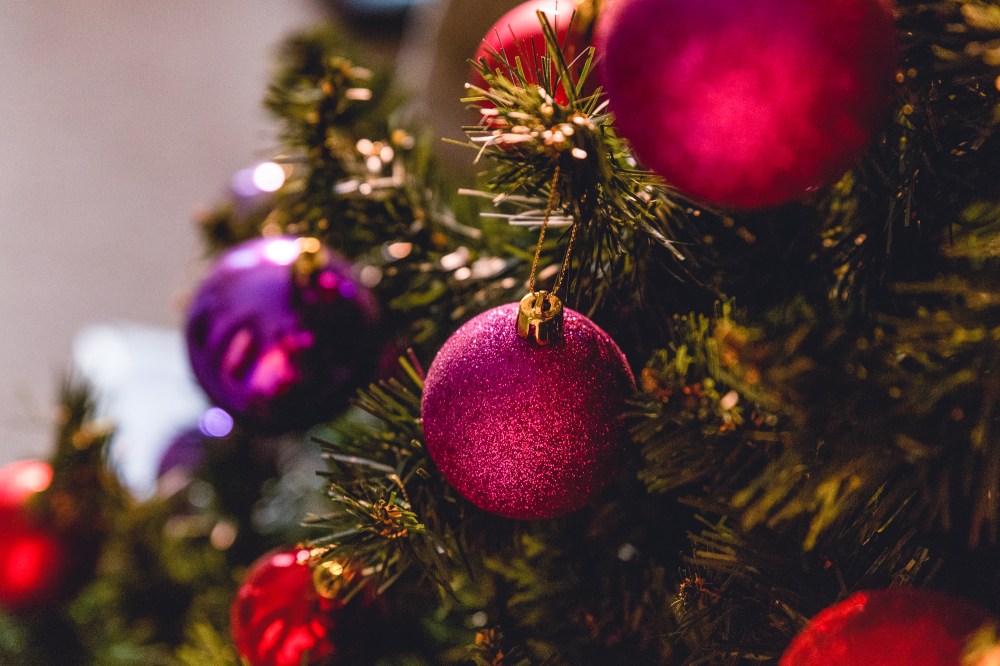 [Image Description: Pink and purple baubles on a green pine Christmas tree with golden light.]