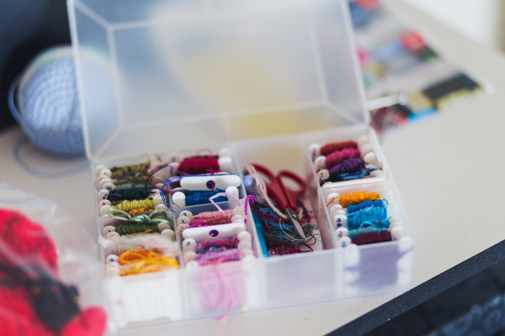 [Image Description: a frosted transparent box filled with embroidery thread on small flat spools and scissors, with other craft supplies around on the white desk.]