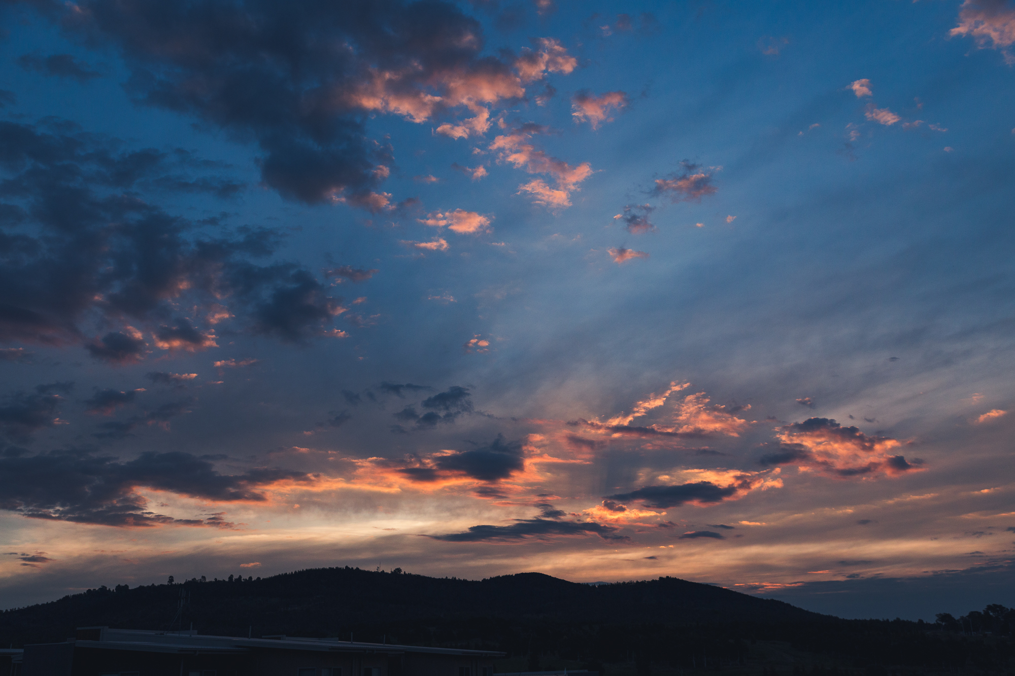 [Image Description: last moments of a sunset, golden light streaking across the sky and lighting up under the clouds, over a dark mountain.]
