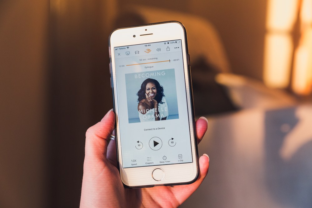 [Image description: iPhone held up with golden sunlit background. The screen shows the audiobook playing Michelle Obama's Becoming book.]